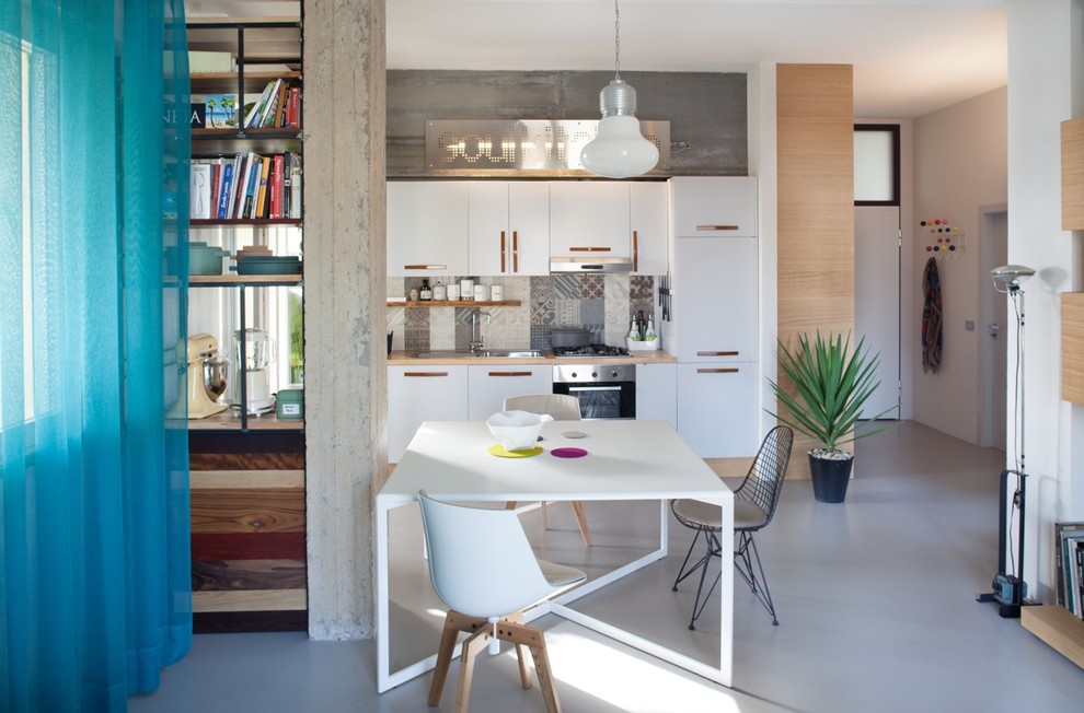 Immagine di una sala da pranzo aperta verso la cucina bohémian con pareti bianche e pavimento in cemento