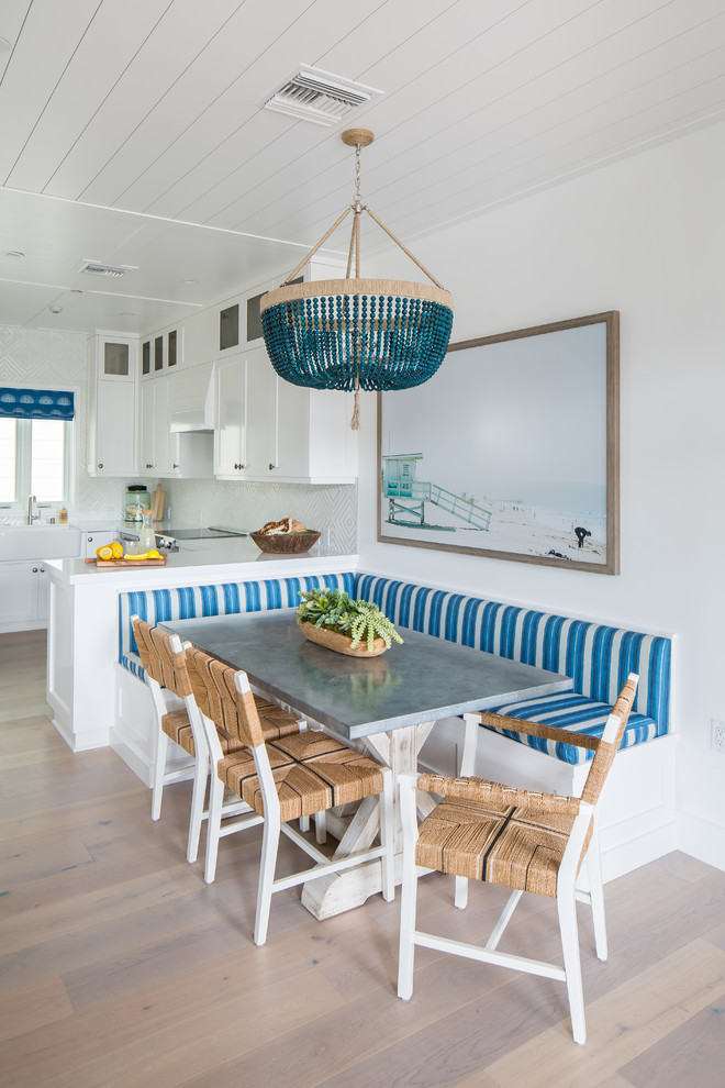 Aménagement d'une salle à manger ouverte sur la cuisine bord de mer avec un mur blanc et parquet clair.