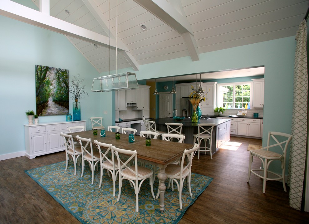 Exemple d'une salle à manger ouverte sur la cuisine bord de mer de taille moyenne avec un mur bleu, un sol en bois brun, une cheminée standard, un manteau de cheminée en pierre et un sol marron.