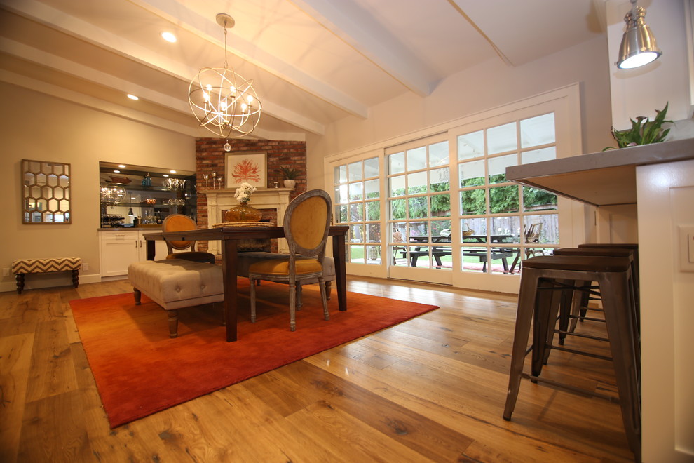 Cette photo montre une grande salle à manger ouverte sur la cuisine moderne avec un mur blanc, un sol en bois brun, une cheminée d'angle et un manteau de cheminée en brique.