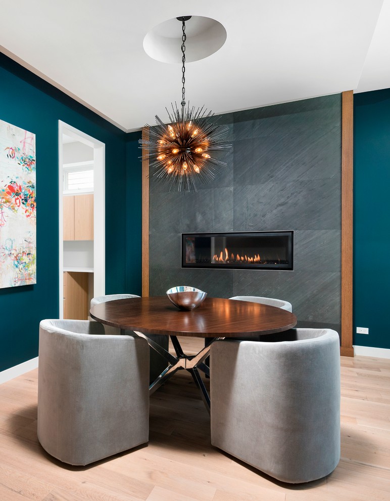 Cette photo montre une salle à manger tendance de taille moyenne avec parquet clair, une cheminée ribbon, un mur bleu et un manteau de cheminée en carrelage.