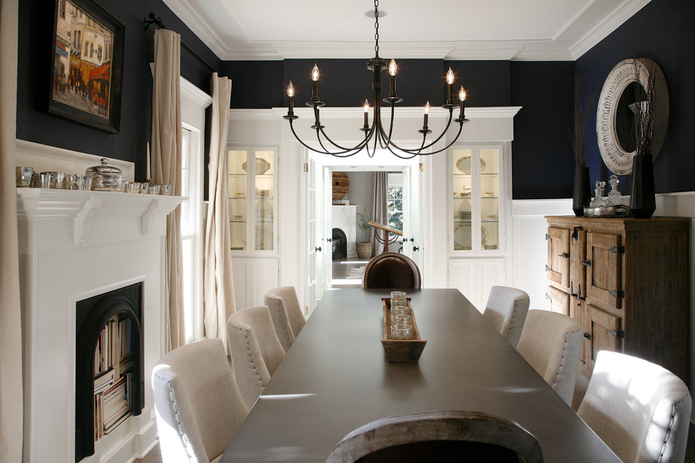 На фото: большая отдельная столовая в стиле неоклассика (современная классика) с стандартным камином, фасадом камина из дерева и черными стенами