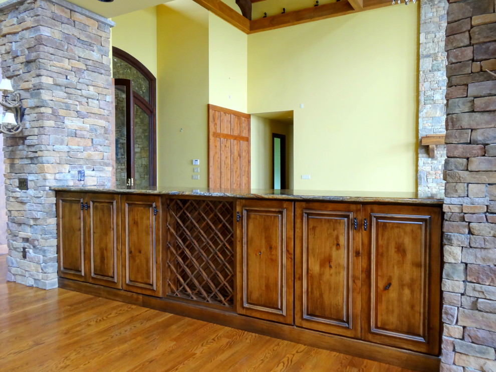 Réalisation d'une très grande salle à manger ouverte sur la cuisine chalet avec un mur jaune, un sol en bois brun, une cheminée standard et un manteau de cheminée en pierre.