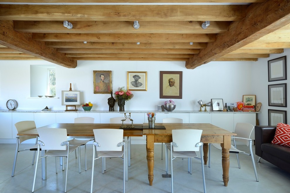 Immagine di una sala da pranzo aperta verso il soggiorno country con pareti bianche, nessun camino e pavimento grigio