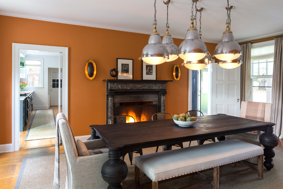 На фото: большая отдельная столовая в стиле неоклассика (современная классика) с оранжевыми стенами, паркетным полом среднего тона, стандартным камином и фасадом камина из камня