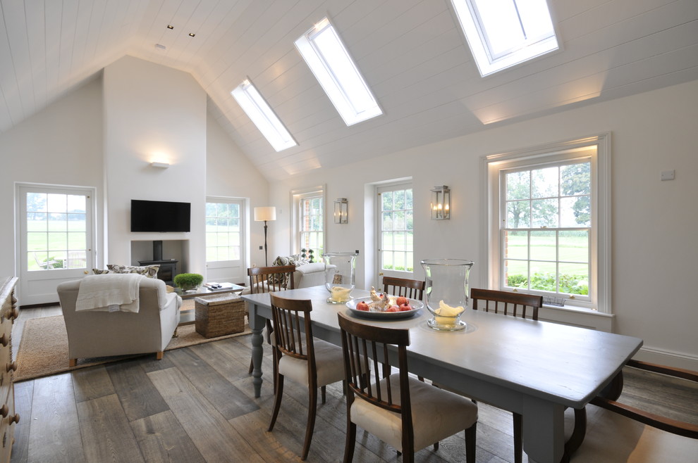 Modelo de comedor de estilo de casa de campo grande abierto con paredes blancas, suelo de madera en tonos medios y estufa de leña