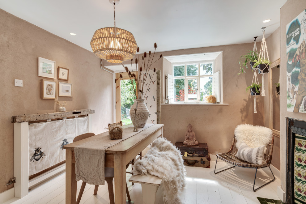 Inspiration for a small eclectic dining room in Cheshire with banquette seating, pink walls, painted wood flooring, a standard fireplace, a plastered fireplace surround and white floors.