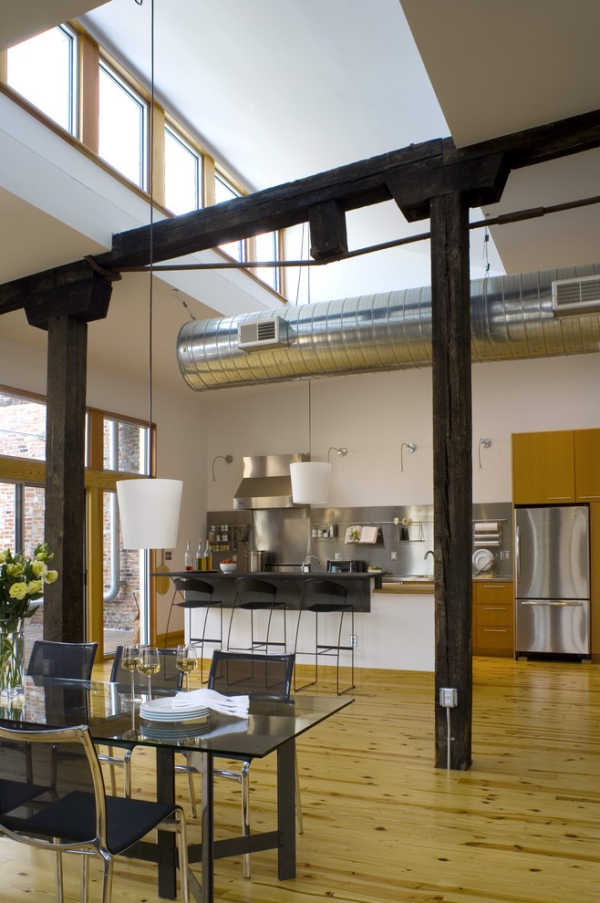 Immagine di una sala da pranzo aperta verso la cucina industriale con parquet chiaro