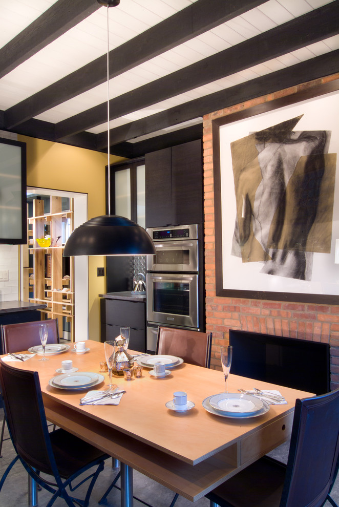 Cette photo montre une salle à manger ouverte sur la cuisine moderne avec un mur jaune, une cheminée standard et un manteau de cheminée en brique.