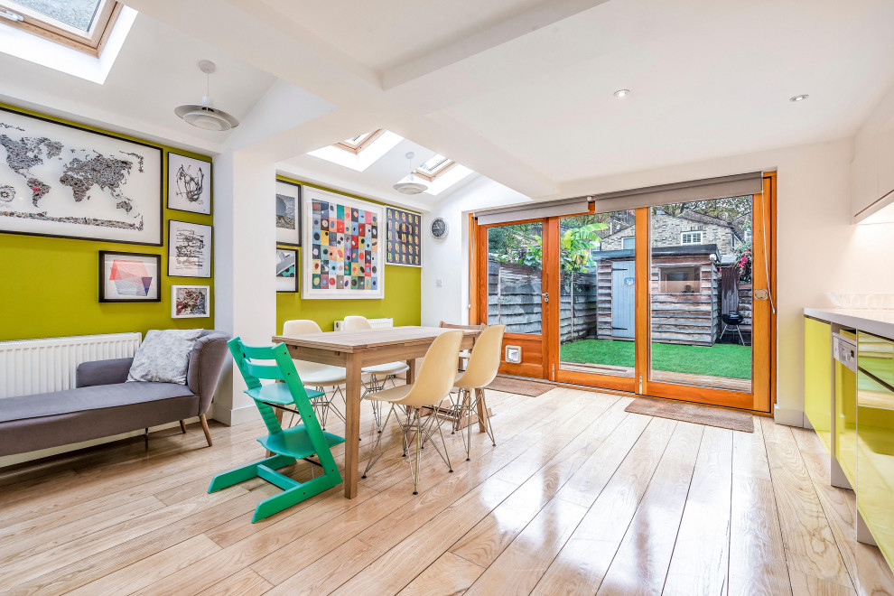 Immagine di una sala da pranzo aperta verso la cucina eclettica con pareti verdi, parquet chiaro e pavimento beige