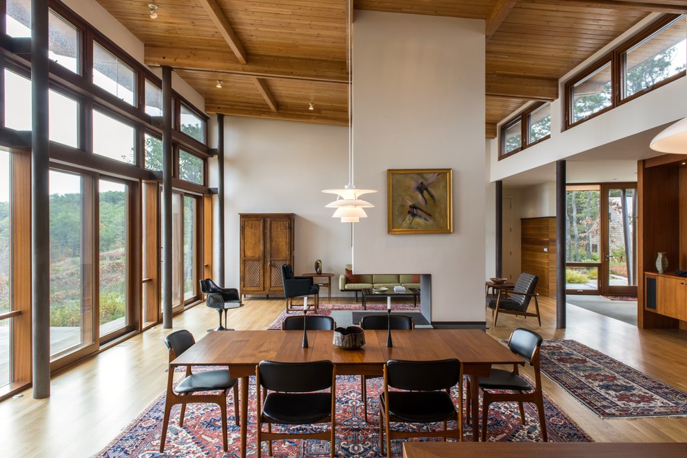 Exemple d'une salle à manger ouverte sur le salon rétro de taille moyenne avec un mur blanc, parquet clair, une cheminée double-face, un manteau de cheminée en béton et un sol marron.