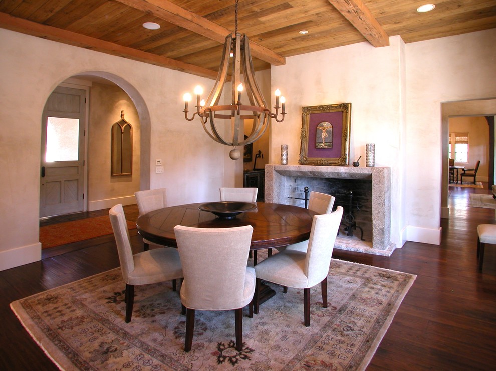 Cette photo montre une grande salle à manger méditerranéenne avec un mur beige, un sol en bois brun, une cheminée standard, un manteau de cheminée en béton et un sol marron.