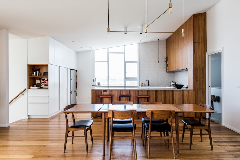 Cette photo montre une salle à manger ouverte sur la cuisine tendance avec un mur blanc, un sol en bois brun et un sol marron.