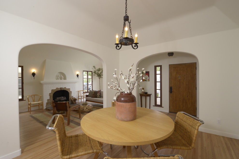 Immagine di una sala da pranzo aperta verso la cucina mediterranea di medie dimensioni con pareti bianche, parquet chiaro, camino classico e cornice del camino piastrellata