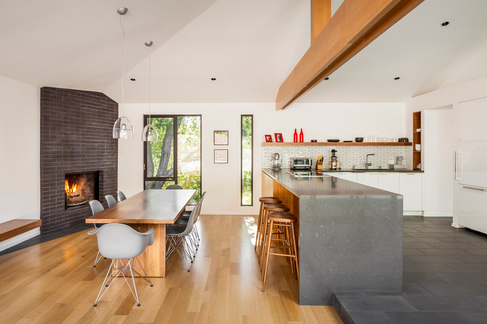 Exempel på en mellanstor minimalistisk matplats med öppen planlösning, med vita väggar, mellanmörkt trägolv, en öppen hörnspis, en spiselkrans i tegelsten och brunt golv