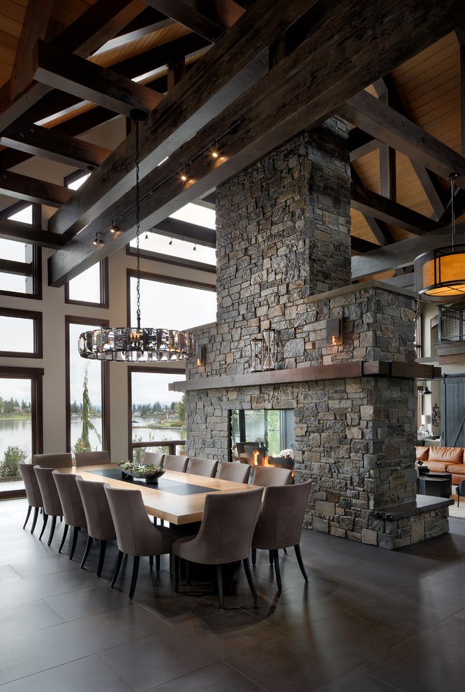 Idées déco pour une salle à manger ouverte sur le salon montagne avec un mur blanc, une cheminée double-face, un manteau de cheminée en pierre et un sol gris.