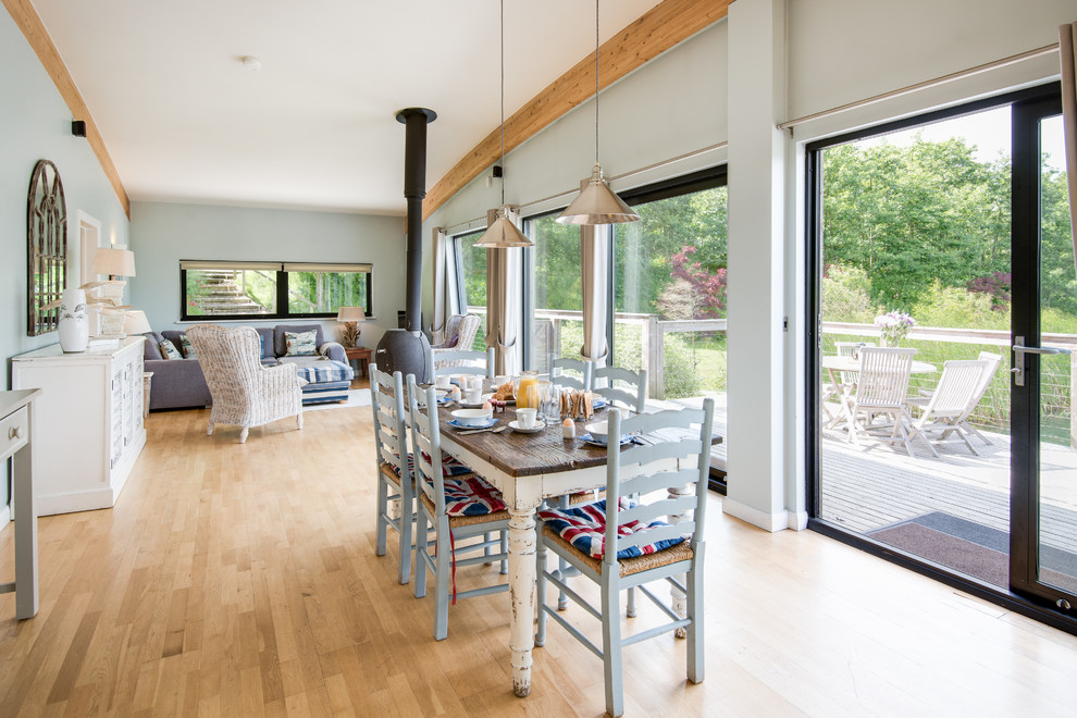 Foto di una grande sala da pranzo aperta verso il soggiorno country con pareti blu, parquet chiaro e stufa a legna