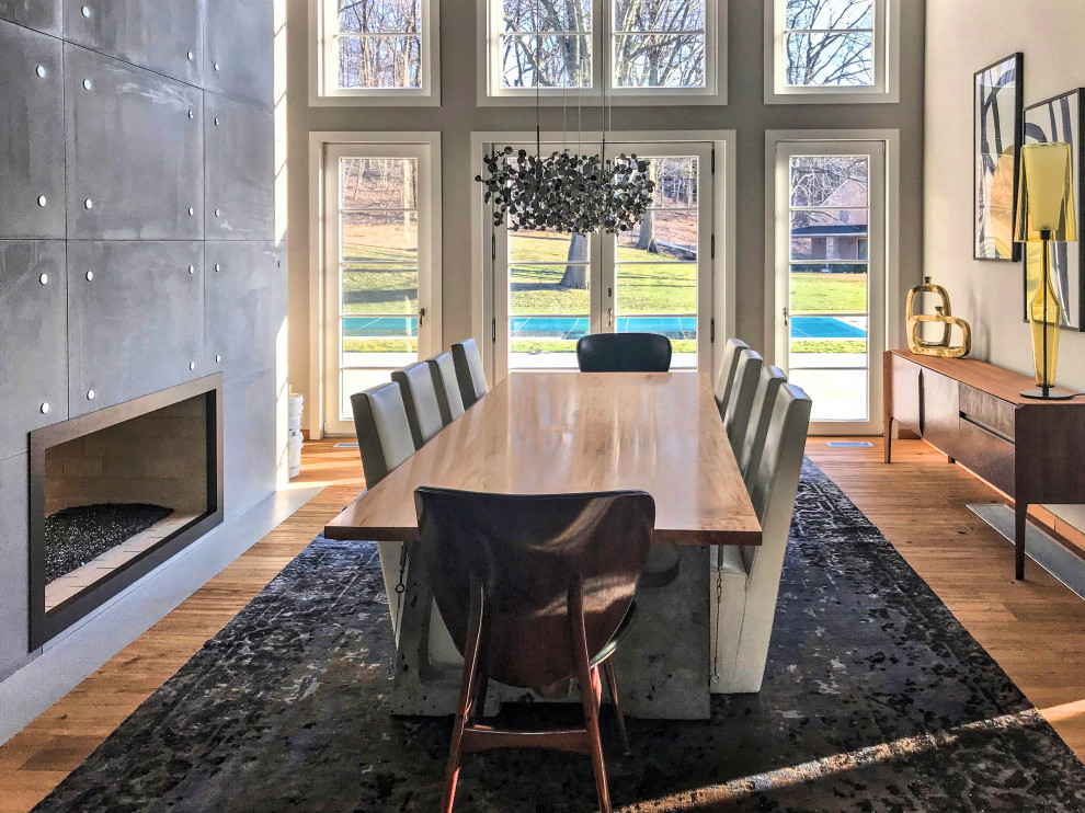 Geräumige Moderne Wohnküche mit grauer Wandfarbe, hellem Holzboden, Tunnelkamin, Kaminumrandung aus Beton und beigem Boden in New York
