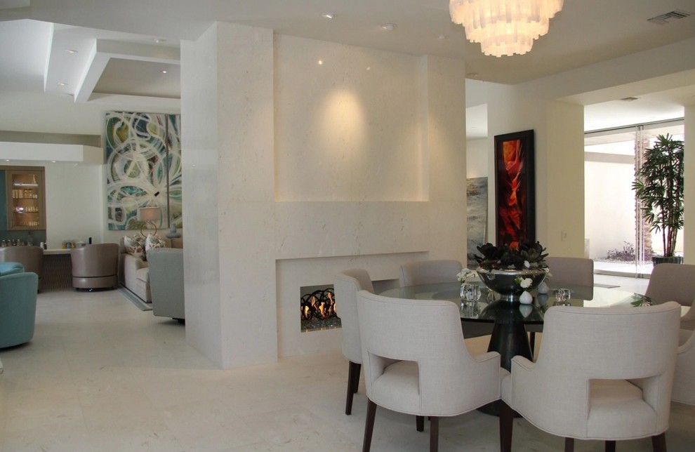 На фото: большая кухня-столовая в современном стиле с белыми стенами, полом из известняка, двусторонним камином и фасадом камина из камня с