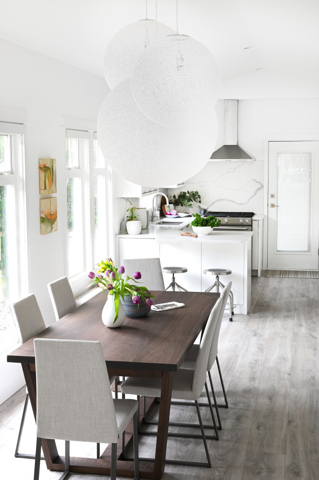 Cette photo montre une petite salle à manger ouverte sur la cuisine moderne avec un mur blanc, sol en stratifié, un sol gris et un plafond voûté.