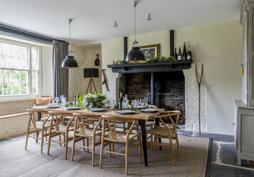 Inspiration for a medium sized farmhouse dining room in Devon with a wood burning stove, black floors, beige walls and feature lighting.