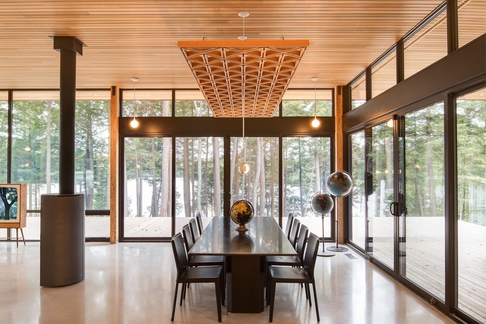 Cette image montre une salle à manger ouverte sur le salon design de taille moyenne avec sol en béton ciré, un poêle à bois, un manteau de cheminée en métal et un sol gris.