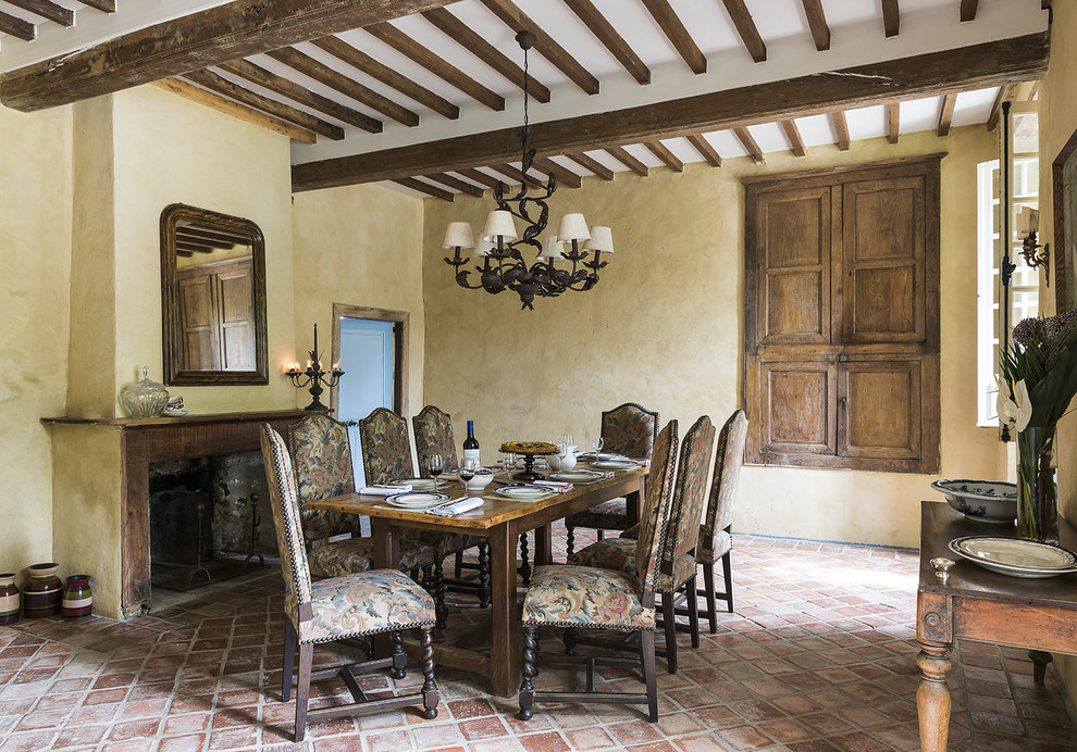 Immagine di una grande sala da pranzo chic chiusa con pareti beige, pavimento in terracotta, camino classico e cornice del camino in pietra