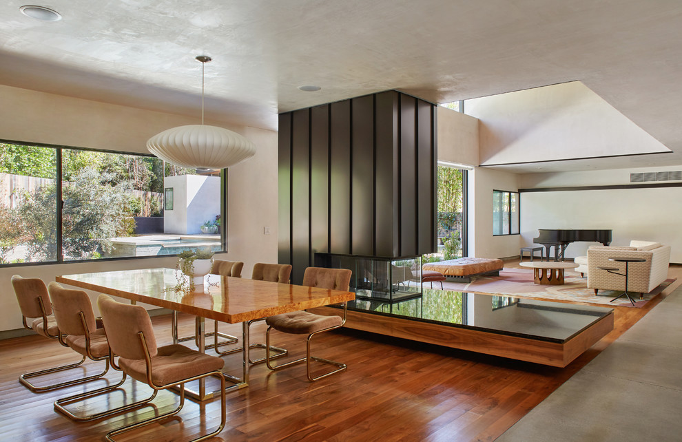 На фото: гостиная-столовая в стиле модернизм с белыми стенами, паркетным полом среднего тона, двусторонним камином, фасадом камина из металла и коричневым полом