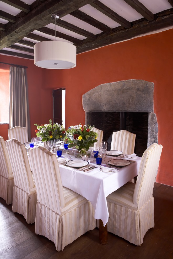 Пример оригинального дизайна: большая отдельная столовая в средиземноморском стиле с темным паркетным полом, фасадом камина из камня, стандартным камином и оранжевыми стенами