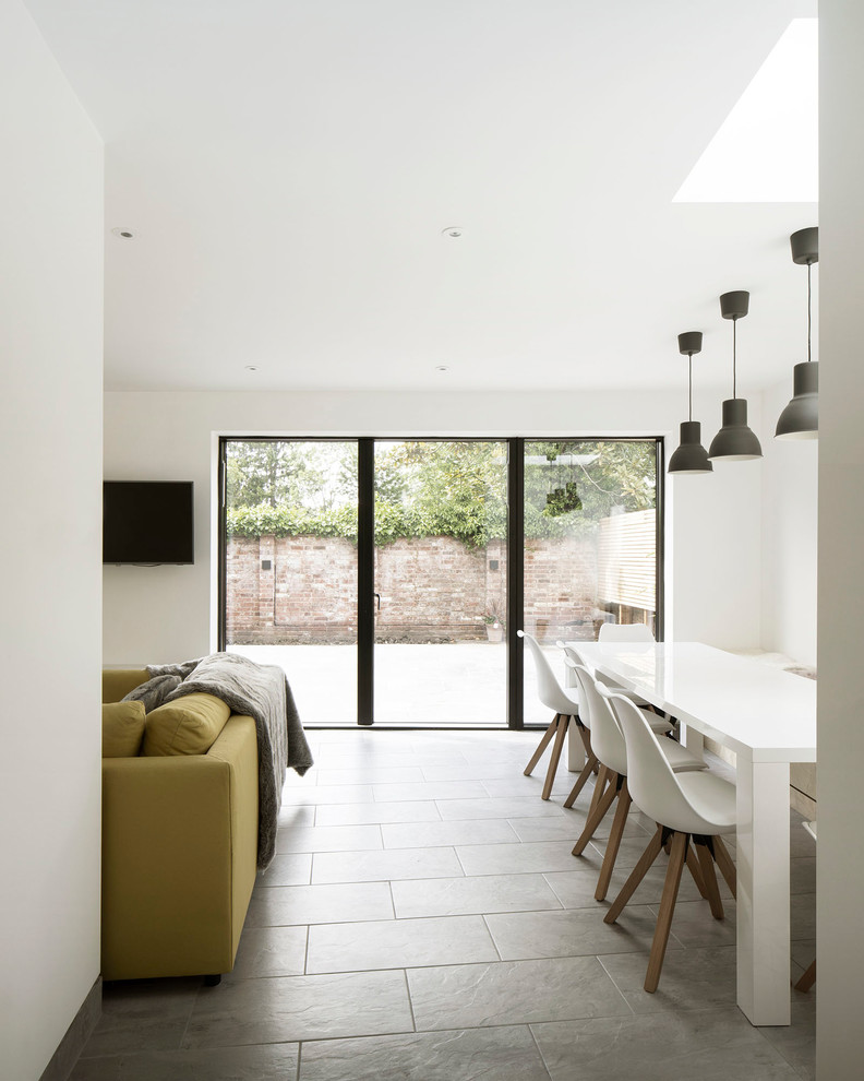 На фото: гостиная-столовая среднего размера в современном стиле с белыми стенами, полом из керамической плитки, печью-буржуйкой, фасадом камина из бетона и серым полом с