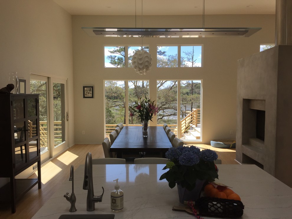 Cette photo montre une salle à manger ouverte sur le salon moderne de taille moyenne avec un mur blanc, parquet en bambou, une cheminée double-face et un manteau de cheminée en béton.