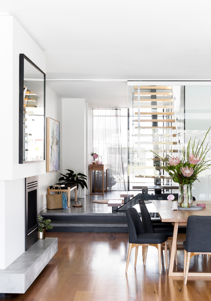 Offenes Modernes Esszimmer mit weißer Wandfarbe, braunem Holzboden, Tunnelkamin, Kaminumrandung aus Beton und braunem Boden in Melbourne