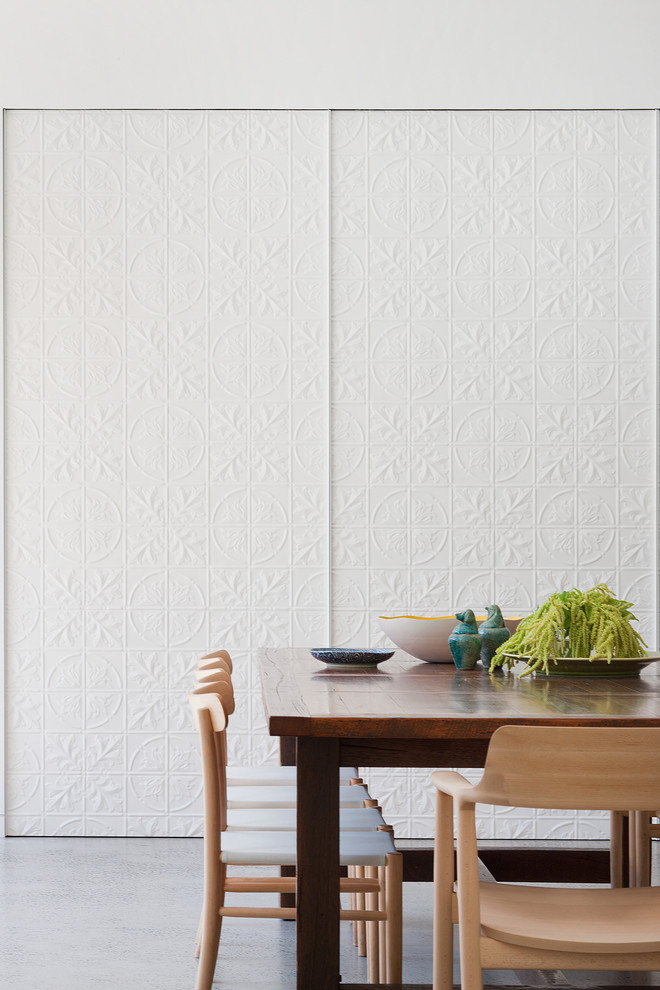 Cette image montre une salle à manger design avec un mur blanc et sol en béton ciré.