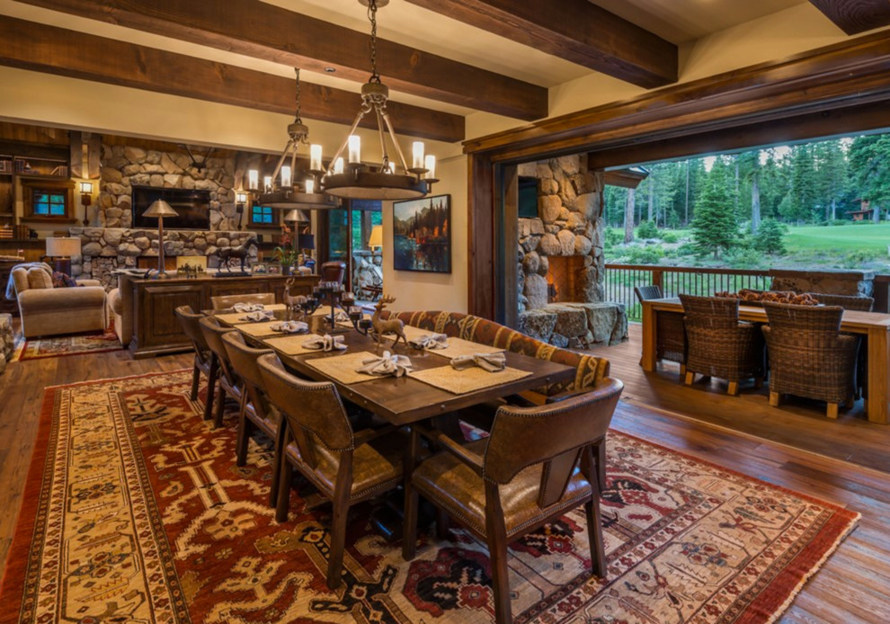 Cette photo montre une salle à manger ouverte sur le salon montagne avec parquet foncé, une cheminée standard et un manteau de cheminée en pierre.