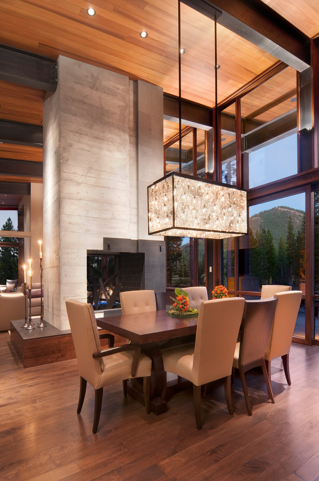Idée de décoration pour une salle à manger ouverte sur le salon chalet avec un manteau de cheminée en béton et une cheminée double-face.
