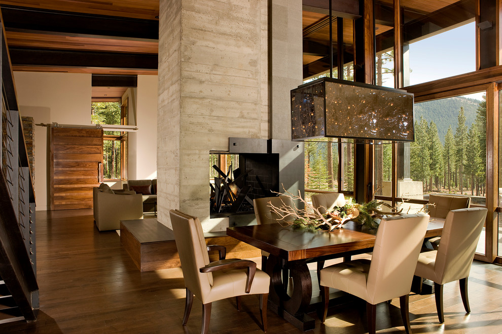 Aménagement d'une grande salle à manger ouverte sur le salon montagne avec un mur beige, un sol en bois brun, une cheminée double-face et un manteau de cheminée en béton.