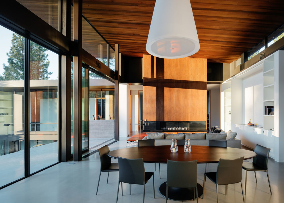 Cette image montre une salle à manger ouverte sur la cuisine design de taille moyenne avec un mur blanc, sol en béton ciré, une cheminée ribbon, un manteau de cheminée en bois et un sol gris.