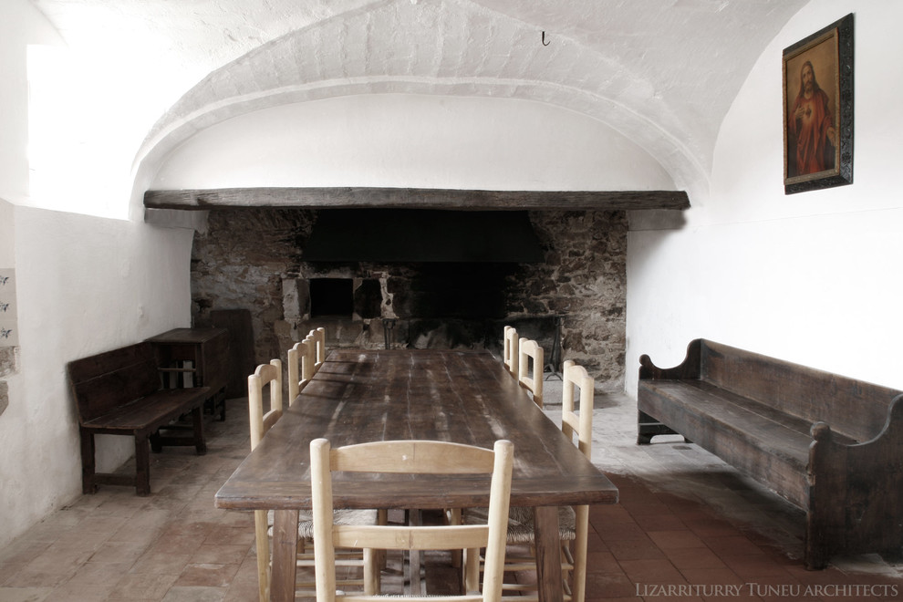 Exemple d'une salle à manger montagne fermée et de taille moyenne avec un mur blanc, tomettes au sol, une cheminée standard et un manteau de cheminée en pierre.