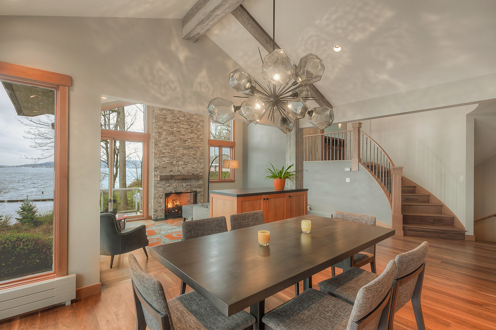 Cette image montre une salle à manger ouverte sur le salon traditionnelle de taille moyenne avec un sol en bois brun, une cheminée standard, un manteau de cheminée en pierre de parement, un sol marron et un plafond voûté.