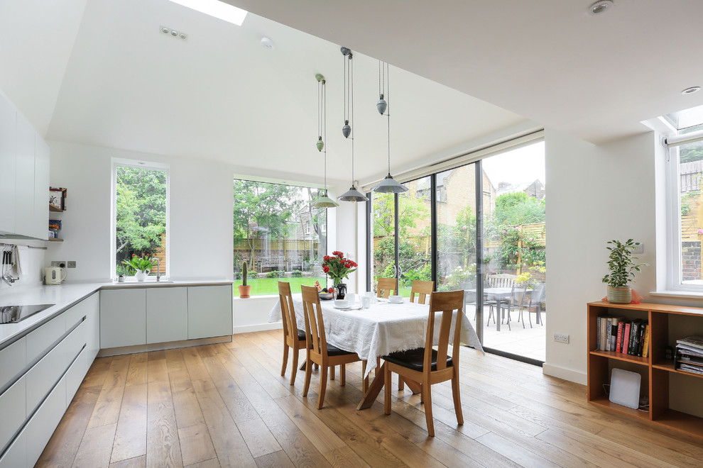 Immagine di una grande sala da pranzo aperta verso la cucina contemporanea con pavimento in legno massello medio, pareti bianche e pavimento marrone