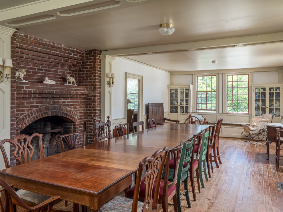 Inspiration pour une très grande salle à manger ouverte sur le salon rustique avec un mur blanc, un sol en bois brun, une cheminée standard et un manteau de cheminée en brique.