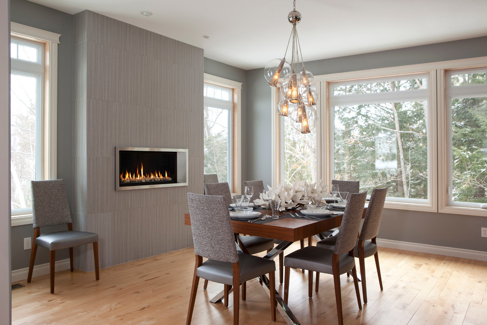 Example of a medium tone wood floor dining room design in Other with gray walls, a ribbon fireplace and a tile fireplace