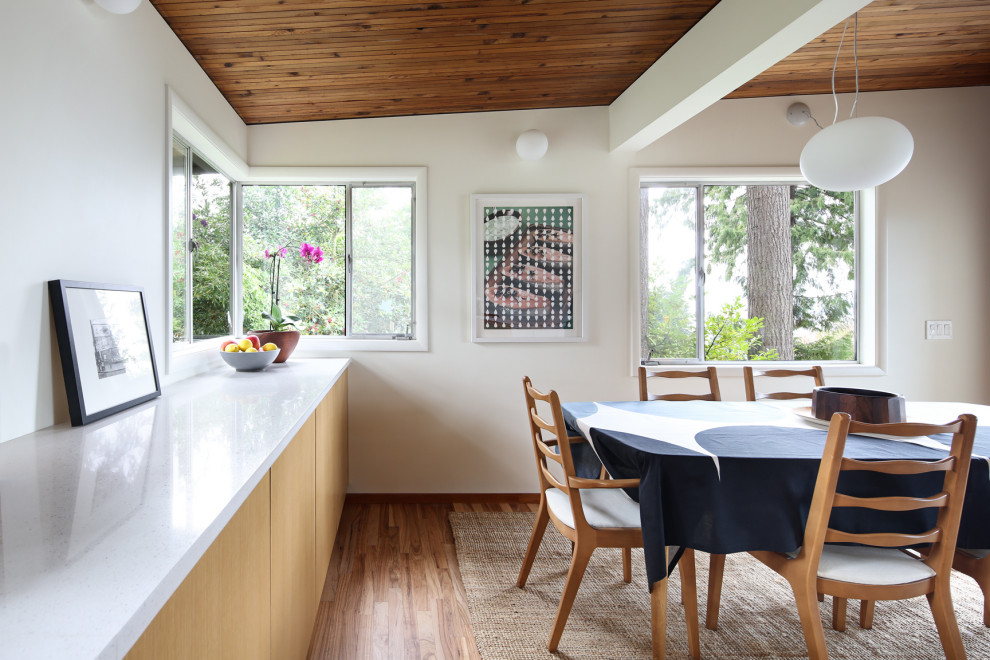 Cette image montre une salle à manger ouverte sur la cuisine vintage de taille moyenne avec un mur blanc, parquet clair, une cheminée d'angle et un manteau de cheminée en brique.