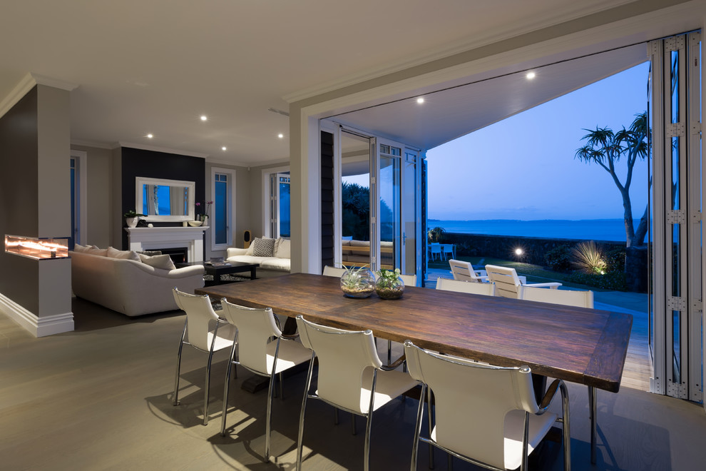 Cette photo montre une grande salle à manger ouverte sur la cuisine bord de mer avec parquet clair, un mur gris et une cheminée double-face.