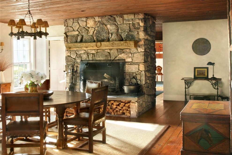 Cette photo montre une salle à manger nature fermée et de taille moyenne avec un mur blanc, un sol en bois brun, une cheminée standard, un manteau de cheminée en pierre et un sol marron.