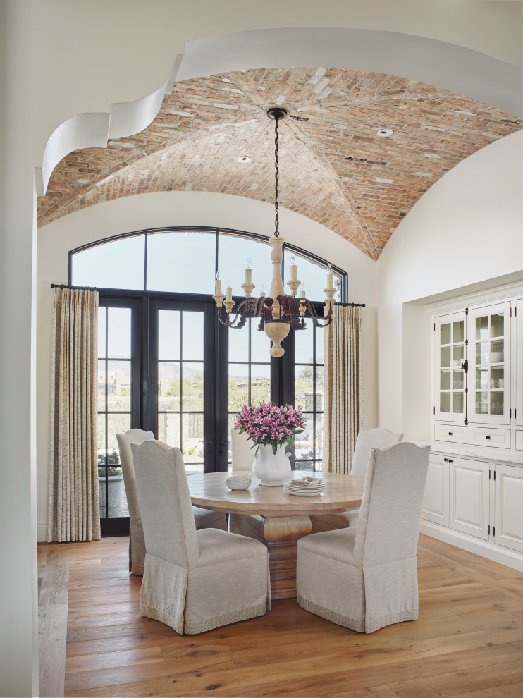 Mediterranean enclosed dining room in Phoenix with white walls, medium hardwood flooring, no fireplace, brown floors and a vaulted ceiling.