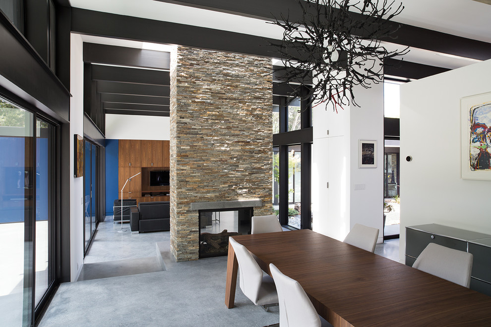 Diseño de comedor actual abierto con paredes blancas, suelo de cemento y chimenea de doble cara