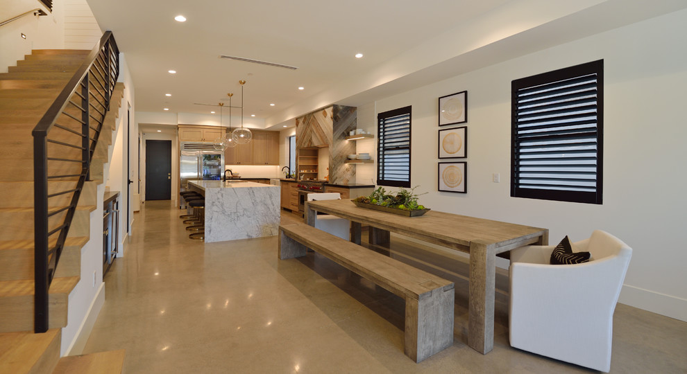 Réalisation d'une salle à manger ouverte sur la cuisine design avec un mur blanc, sol en béton ciré et un sol gris.