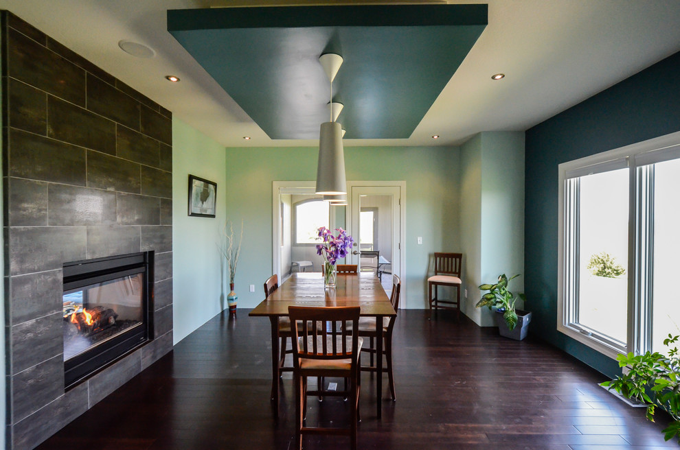 На фото: большая кухня-столовая в стиле модернизм с синими стенами, темным паркетным полом, двусторонним камином и фасадом камина из плитки