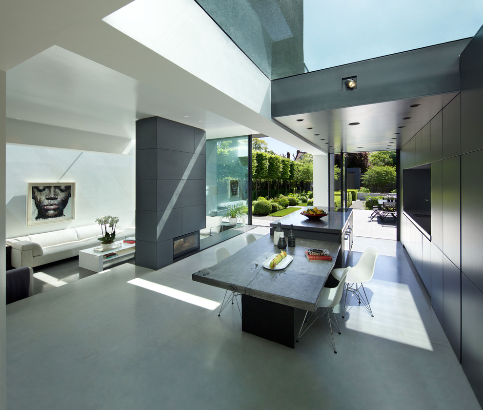 Photo of a large modern dining room in London with white walls, concrete flooring, a standard fireplace and grey floors.